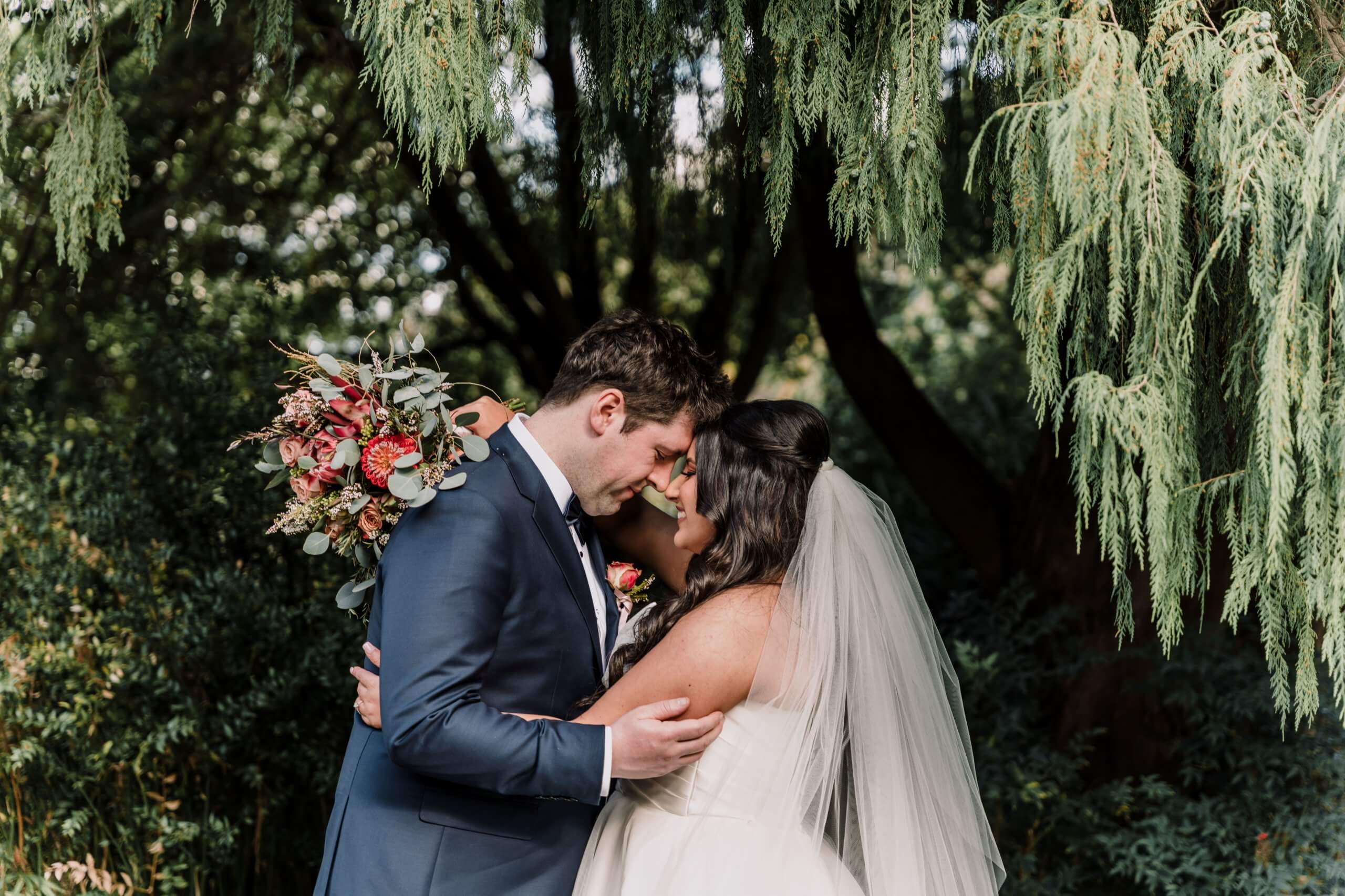Nose to nose, arm in arm - the bride and groom embraces each other while they are surrounded by greenery.