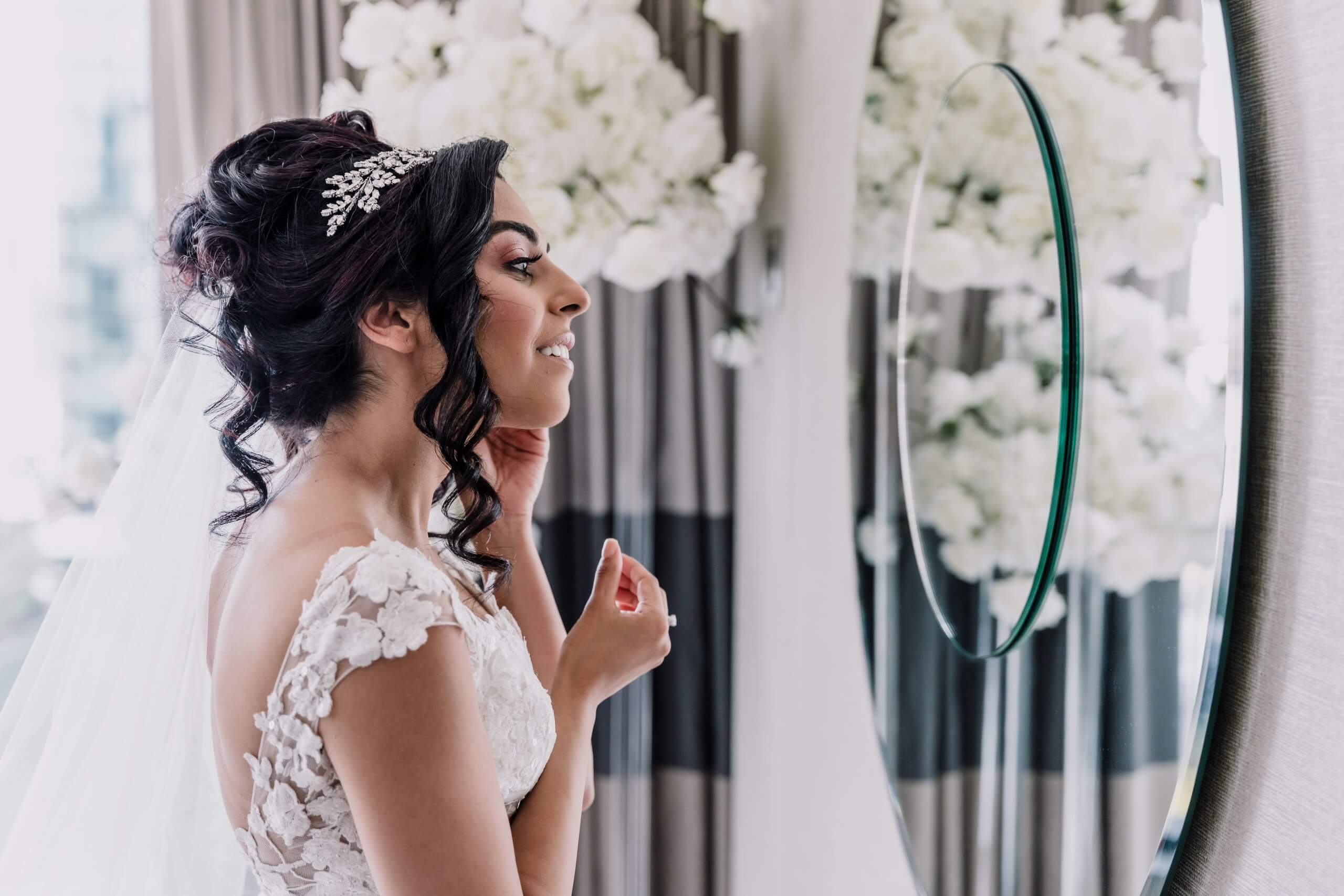 Profile shot of the bride donning her earrings in front of a mirror.