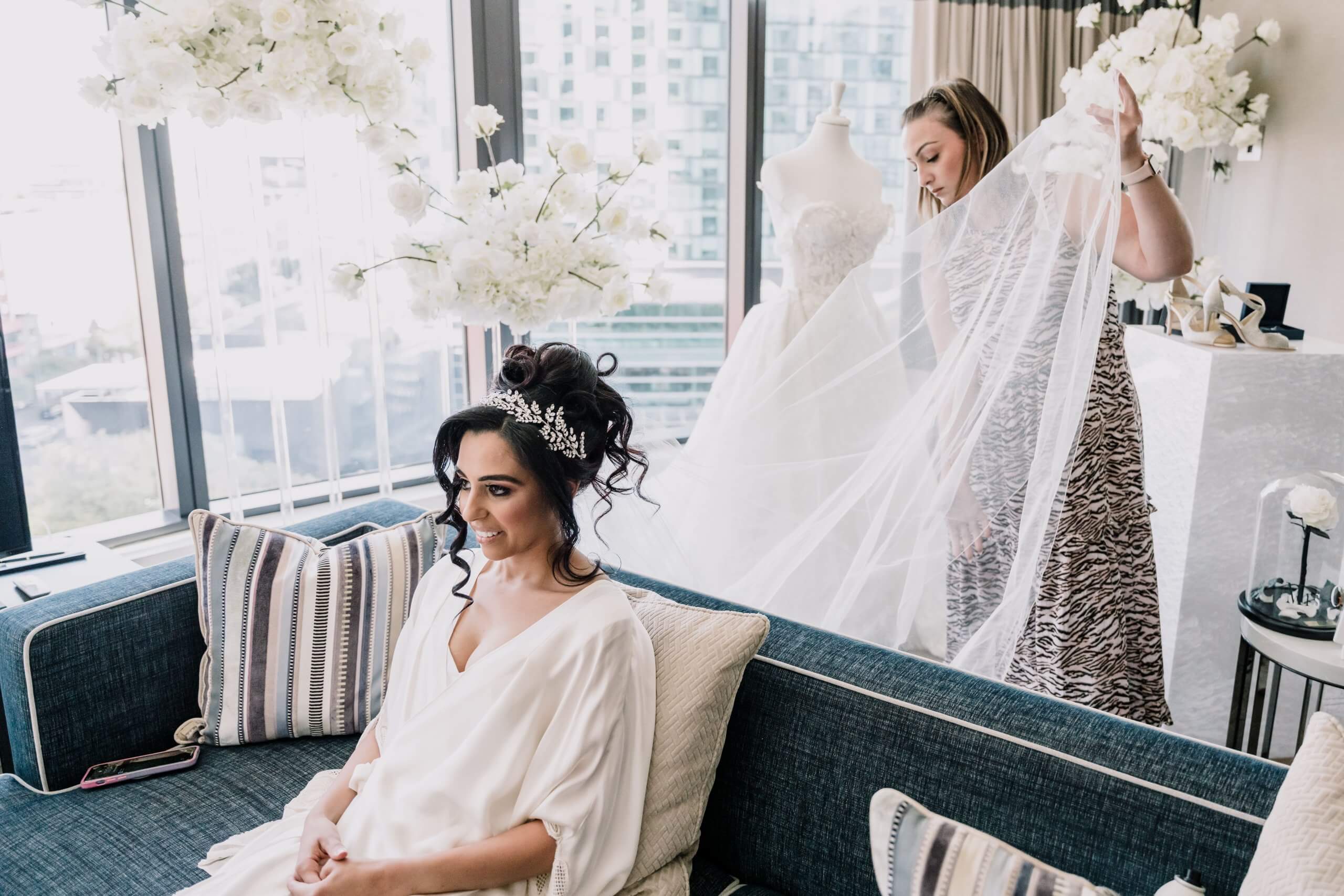 The bride is sitting on a couch, wearing her wedding robe and getting ready.