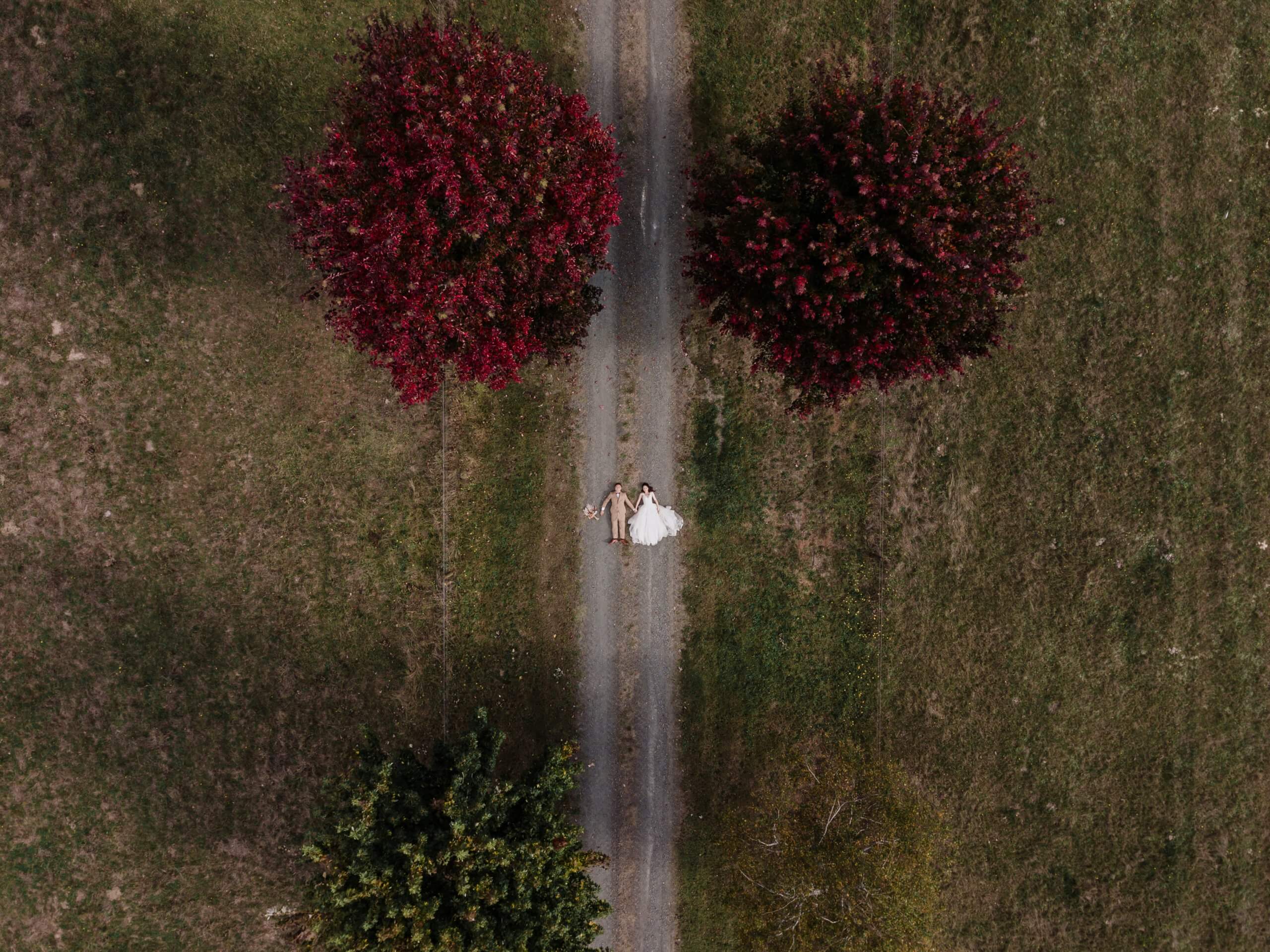 Longshot photo of the bride and groom captured by the drone as they lie down in the middle of the road