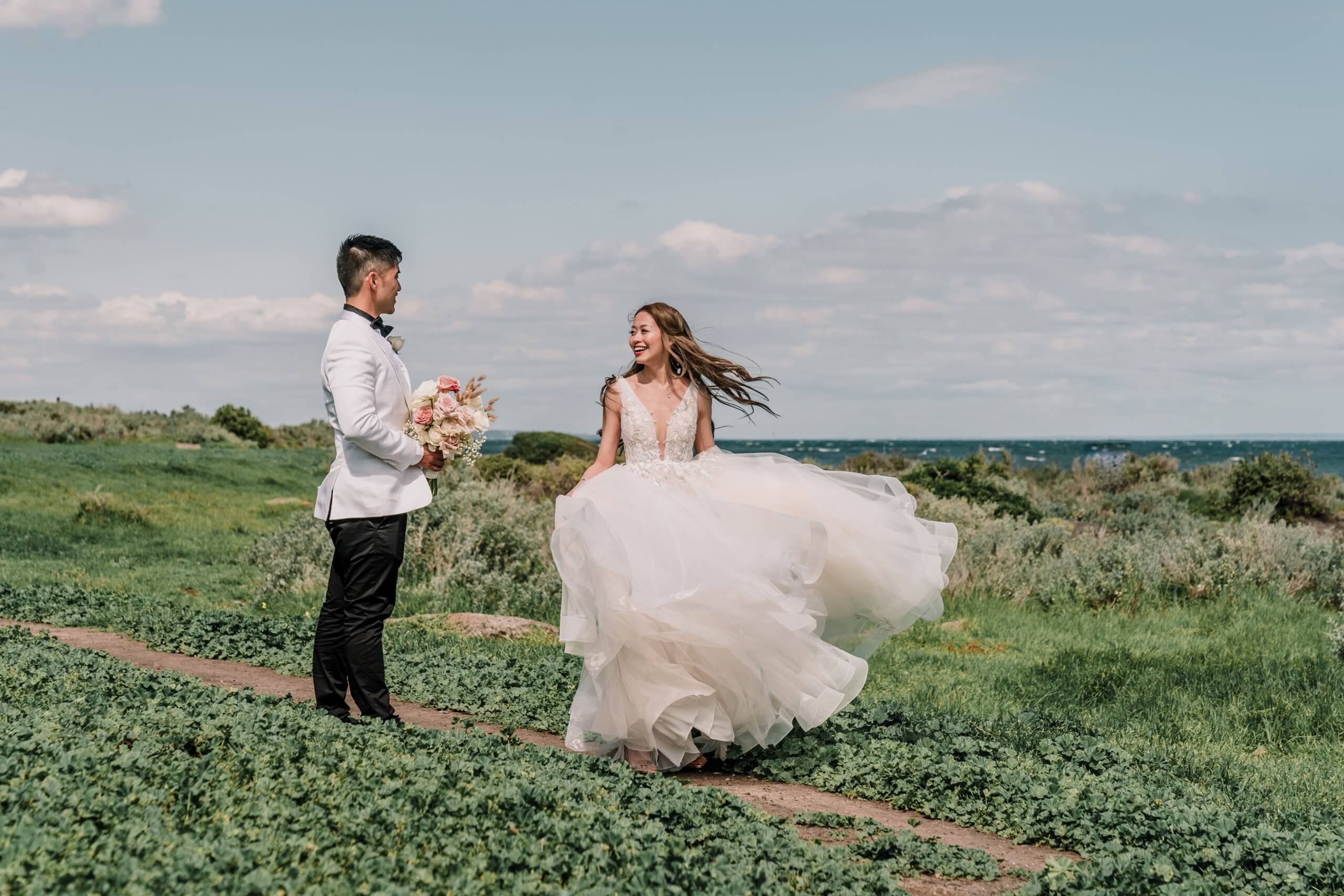Candid photo of the bride dancing while her groom looks at her - with the sea as the background
