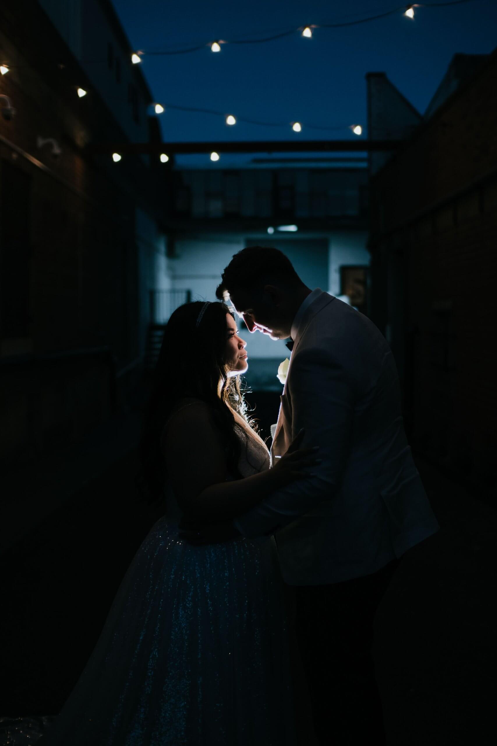 Beautiful photo captured during the night. The bride and groom's side profile silhouette is illuminated by artificial light placed in between them.