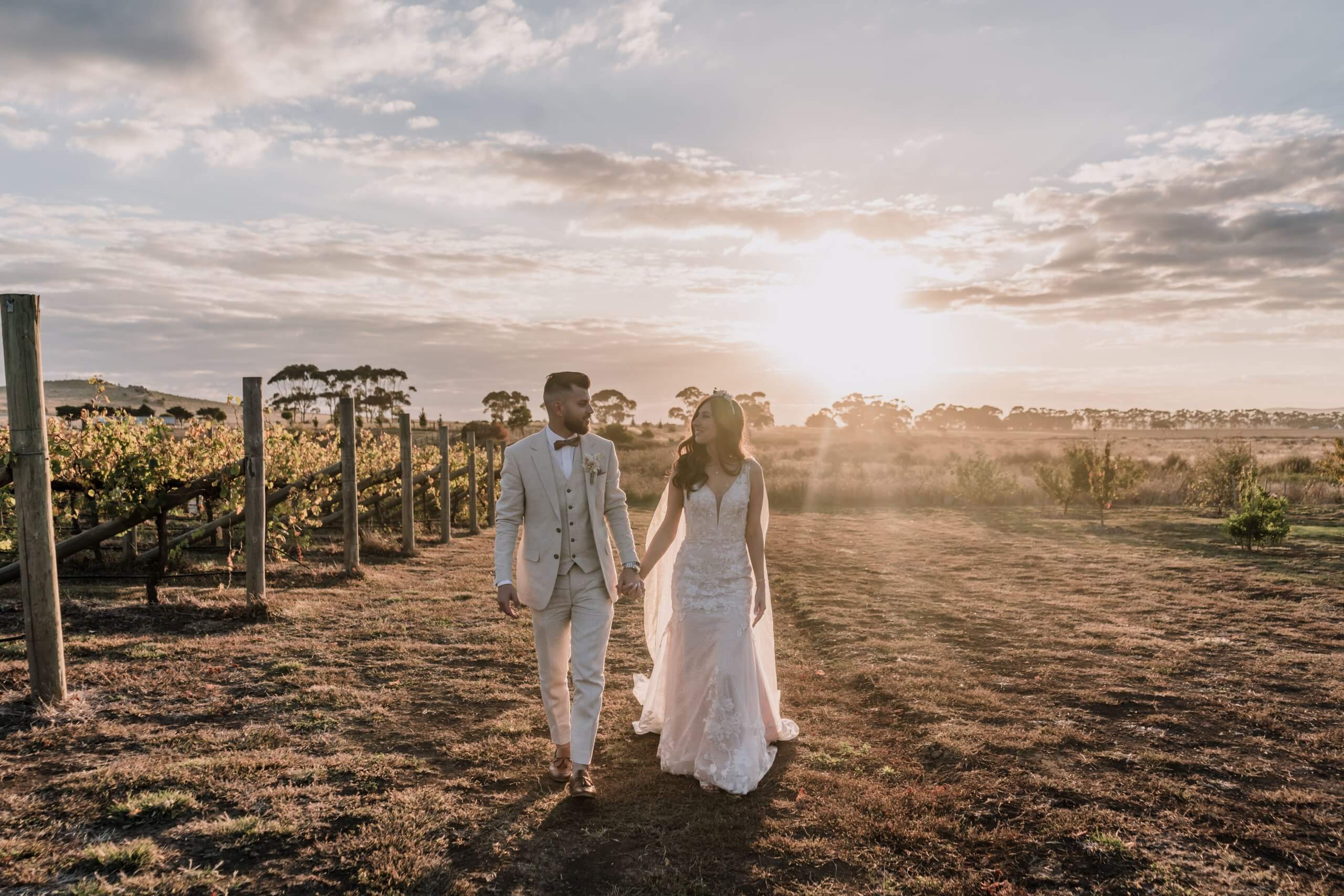 Bride and groom walking hand in hand in the middle of the winery and with the setting sun accentuating their silhouette.