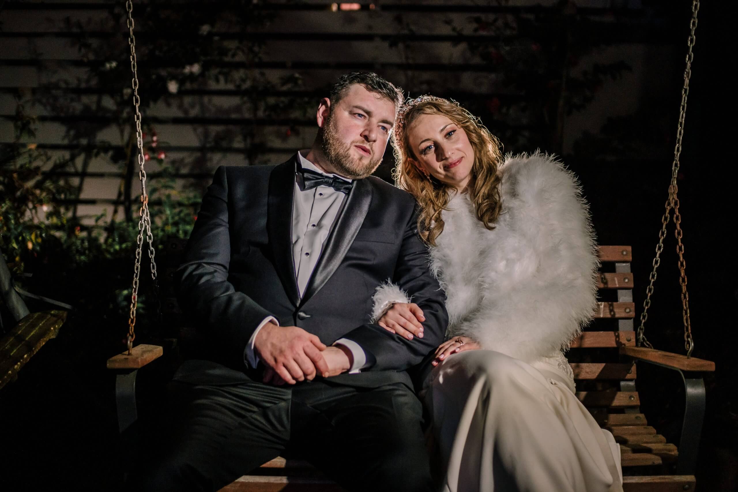 Nighttime photo of the bride and grooms who sits together on a wooden swing.