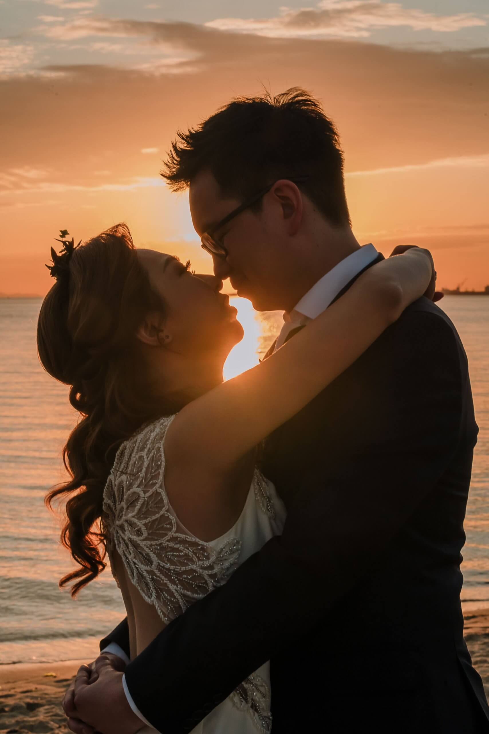 With the sea and the sunset as the backdrop, the bride and groom embraces each other lovingly.