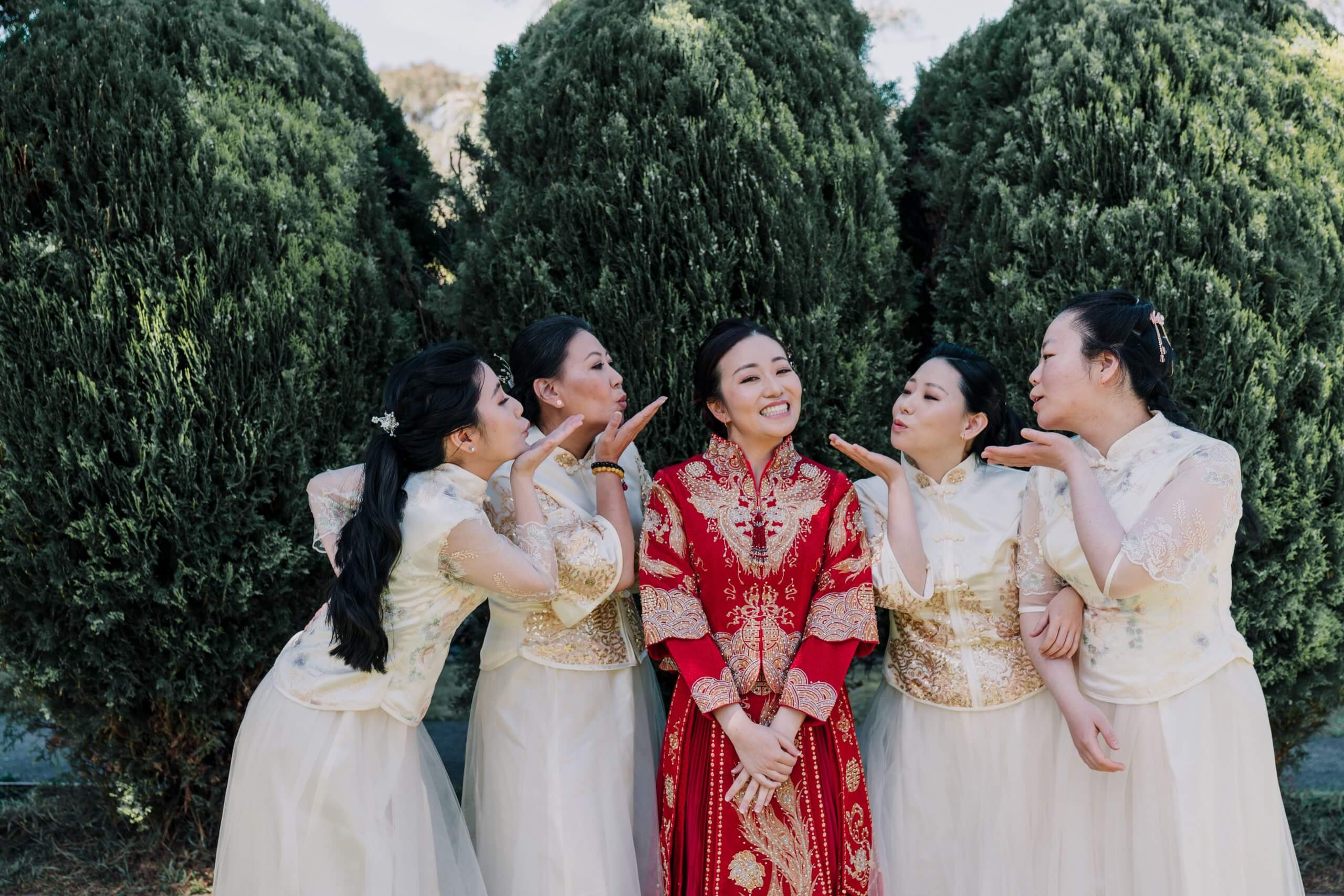 Customise Your Wedding - Bride wearing a traditional Chinese wedding dress, surrounded by her 4 bridesmaids who are blowing her kisses.