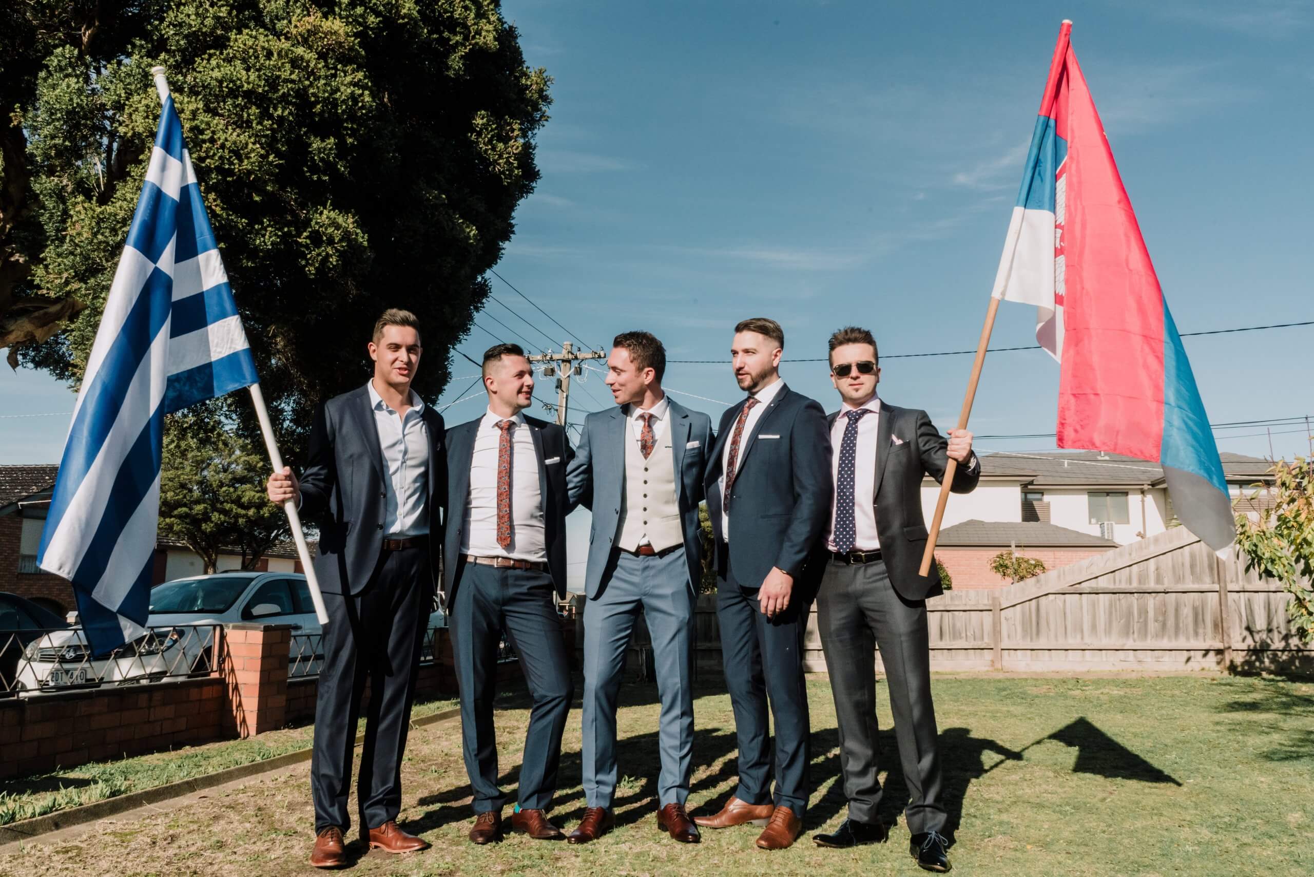 Customise Your Wedding - The groom stands between four groomsmen. The two groomsmen on both ends each holding the Flags of Greece and Serbia.