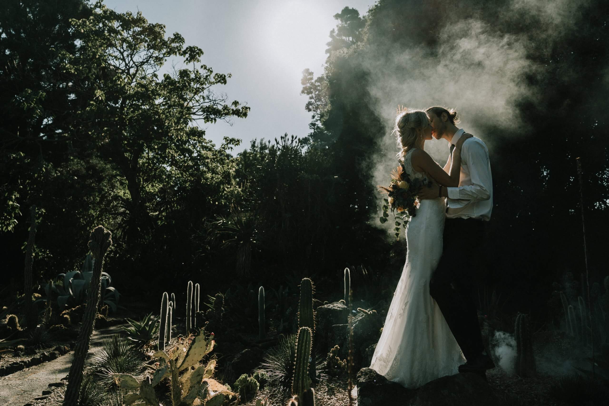 Narrative Portraiture - The bride and groom share a kiss in front of a dark, foggy forest
