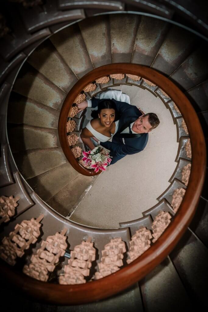 Narrative Portraiture - The bride and groom looking up from the bottom of a spiral staircase