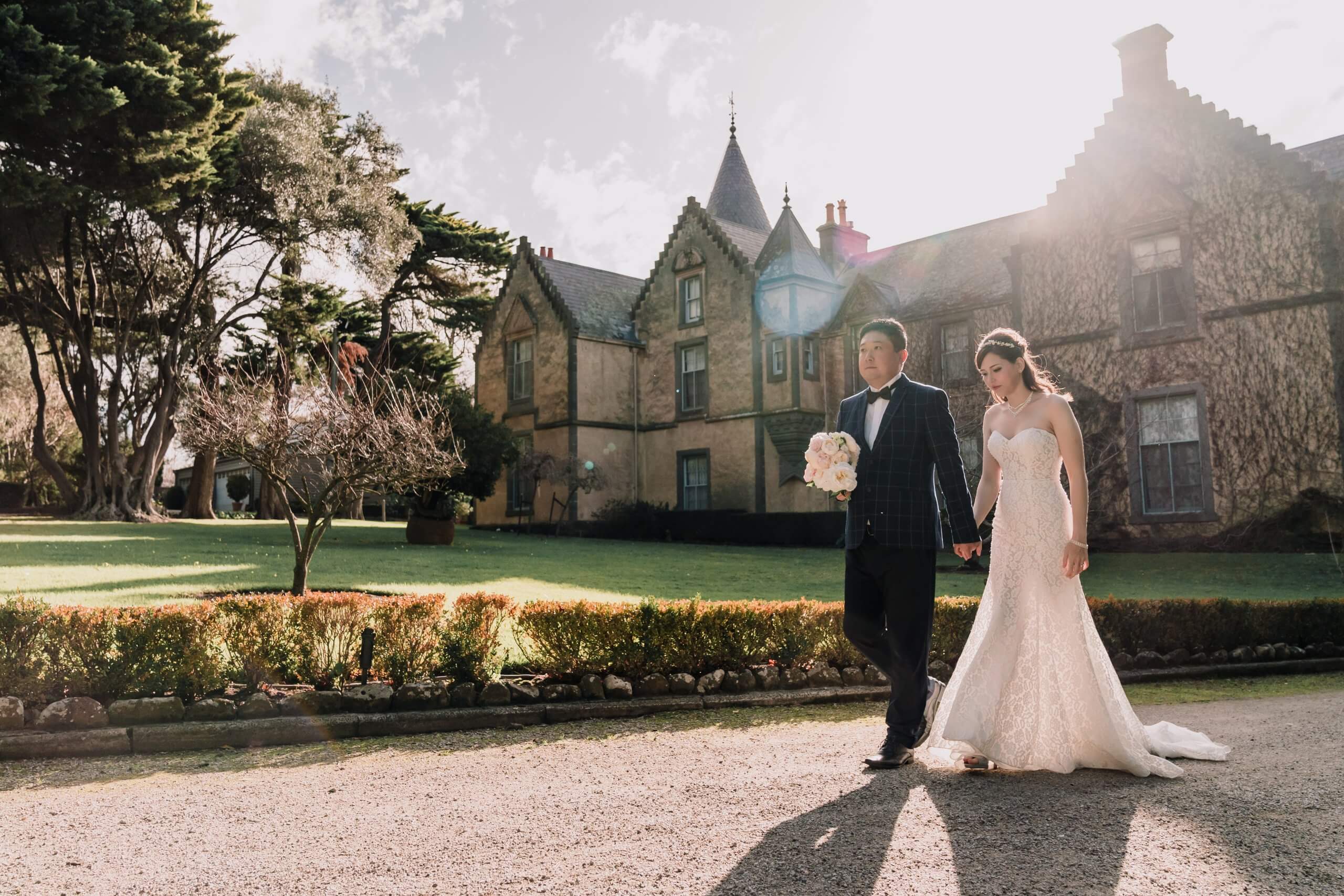 A groom and bride strolling through Overnewton Castle's paths.