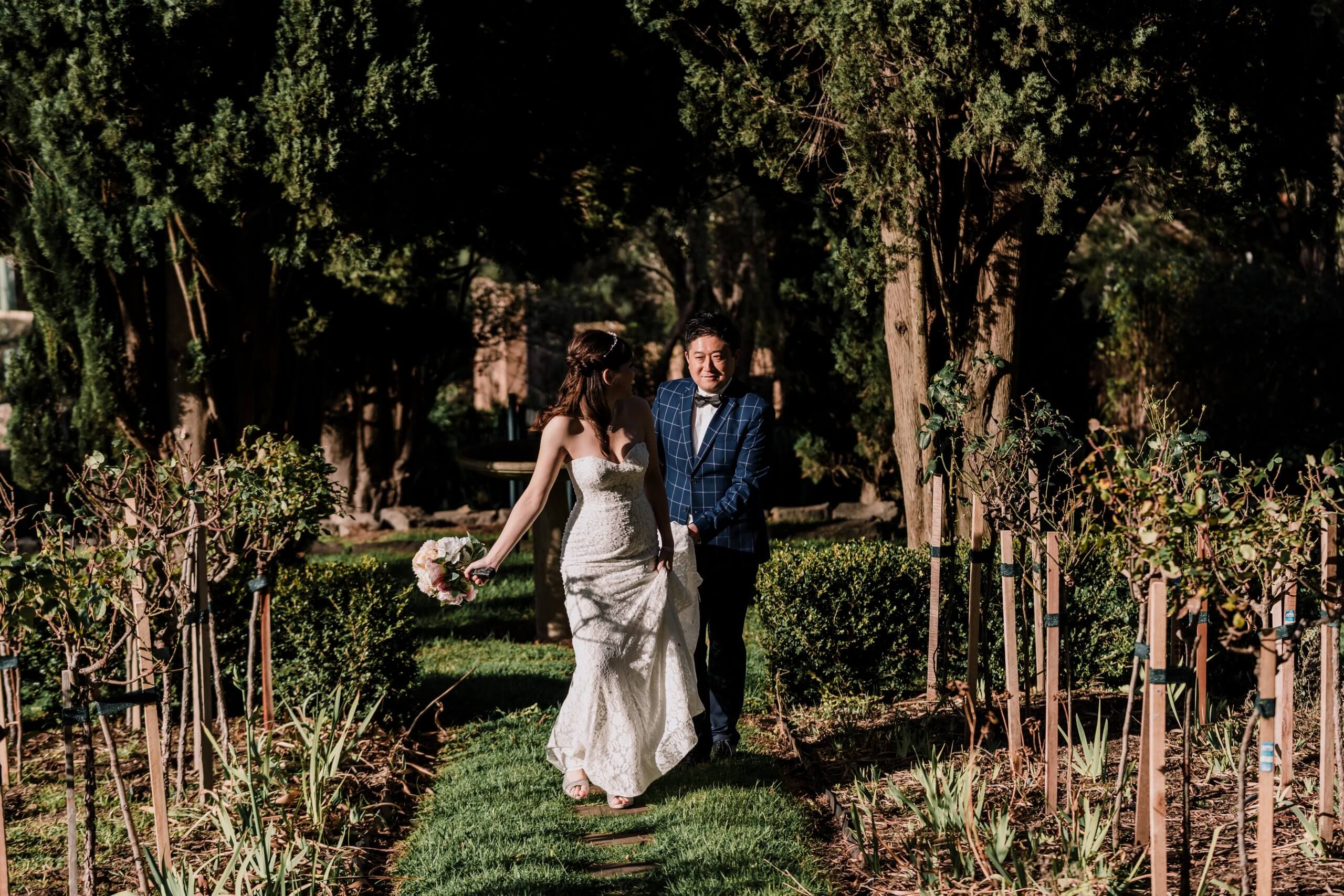 The bride and groom running away along the greenery of Overnewton Castle