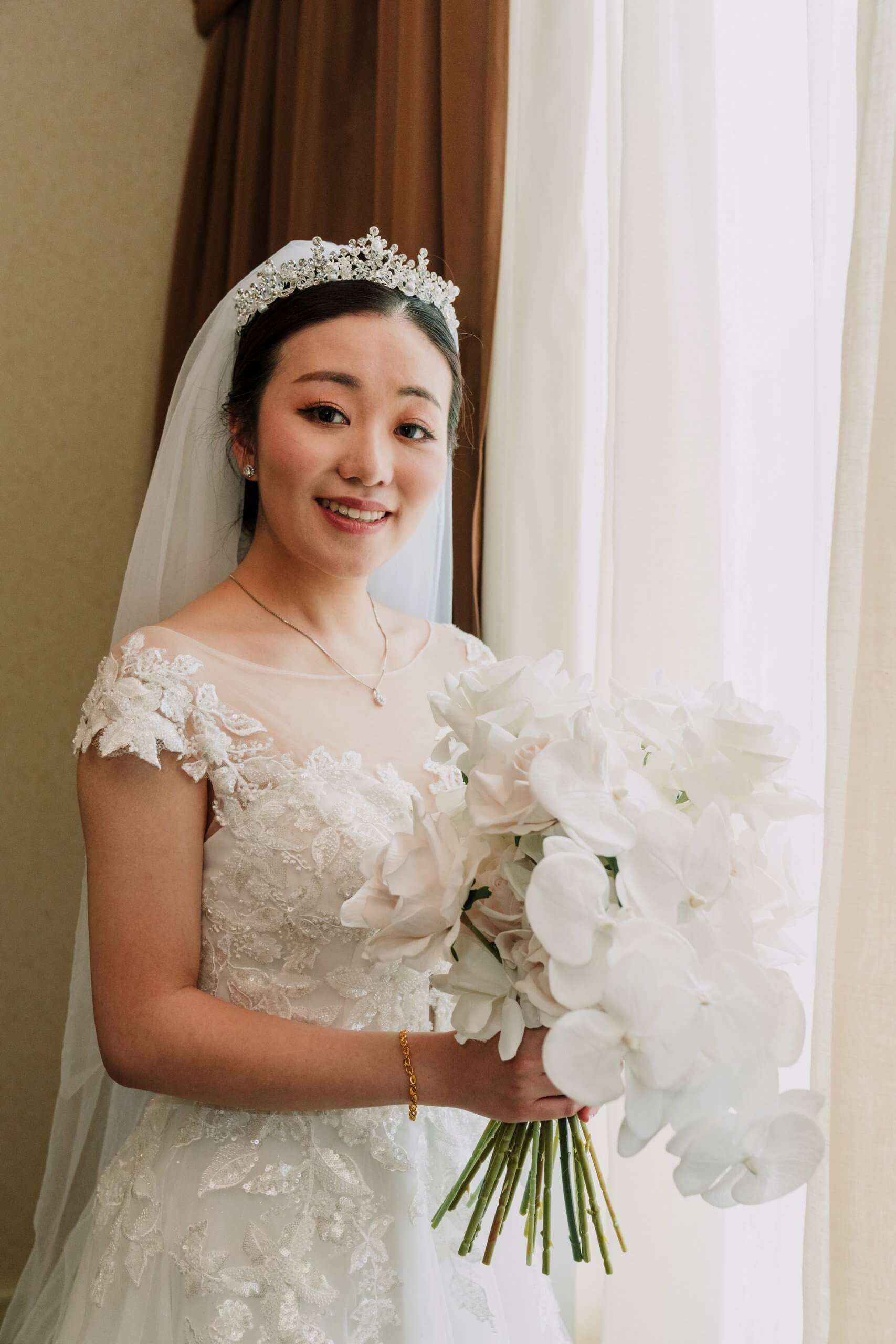 Bride standing by a window, holding her bouquet and smiling